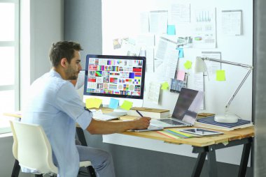 İnternette çalışırken bilgisayarın ve dizüstü bilgisayarın önünde grafik stüdyosunda oturan genç tasarımcının portresi.