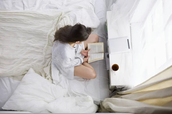 Woman sitting in bed reading a book and having breakfast — Stock Photo, Image