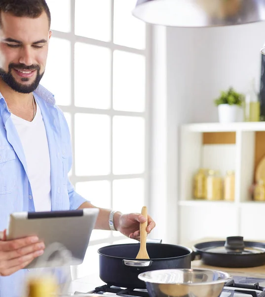 Hombre siguiendo la receta en la tableta digital y cocinar comida sabrosa y saludable en la cocina en casa — Foto de Stock