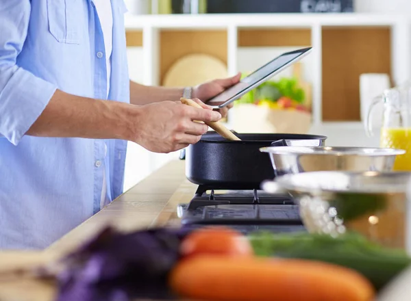 Man following recipe on digital tablet and cooking tasty and healthy food in kitchen at home — Stock Photo, Image