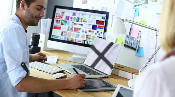 Retrato del joven diseñador sentado en el estudio gráfico frente a la computadora portátil y el ordenador mientras trabaja en línea. — Foto de Stock