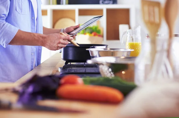 Man following recipe on digital tablet and cooking tasty and healthy food in kitchen at home — Stock Photo, Image