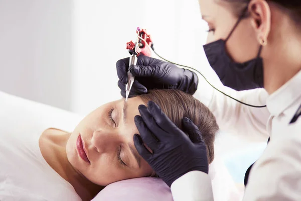 Jonge vrouw ondergaat procedure van wenkbrauw permanente make-up in schoonheidssalon — Stockfoto