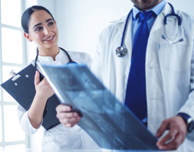 İki doktor röntgen görüntülerini inceliyor, parlak ofiste danışmanlık yapıyorlar.