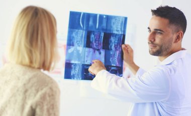 Yakışıklı doktor genç bayan hastasıyla konuşuyor ve ofisinde otururken notlar alıyor..