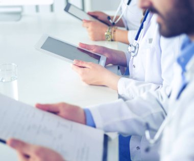 Toplantıdaki doktorlar, masanın üstünde oturuyorlar.