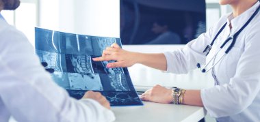 İki doktor röntgen görüntülerini inceliyor, parlak ofiste danışmanlık yapıyorlar.