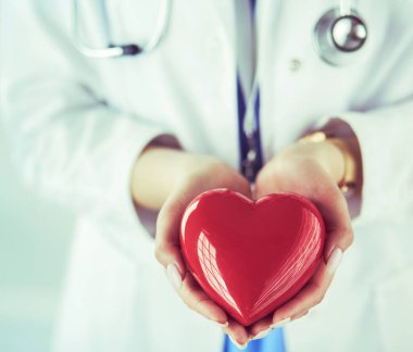 Steteskop tutan, kalbi hafif arka planda olan kadın bir doktor.