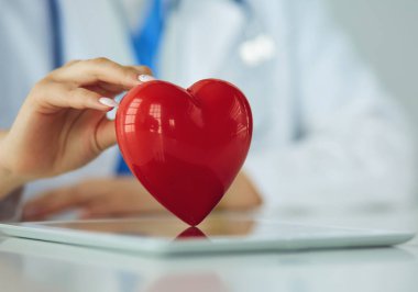 Steteskop tutan, kalbi hafif arka planda olan kadın bir doktor.