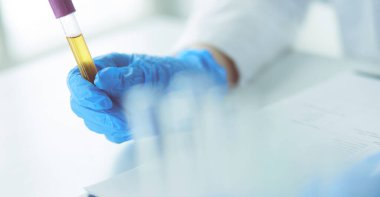 Kadın araştırmacı, beyaz arka planda izole edilmiş ilaç şişeleri ve mataralarla çevrili.