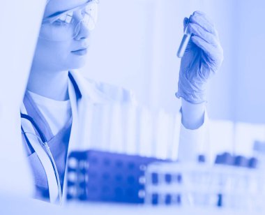 Kadın araştırmacı, beyaz arka planda izole edilmiş ilaç şişeleri ve mataralarla çevrili.