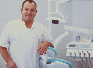 Diş kliniğinde duran gülümseyen bir dişçinin portresi.