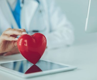 Steteskop tutan, kalbi hafif arka planda olan kadın bir doktor.