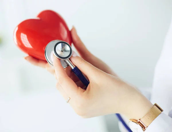 Um médico com estetoscópio examinando coração vermelho, isolado em fundo branco — Fotografia de Stock