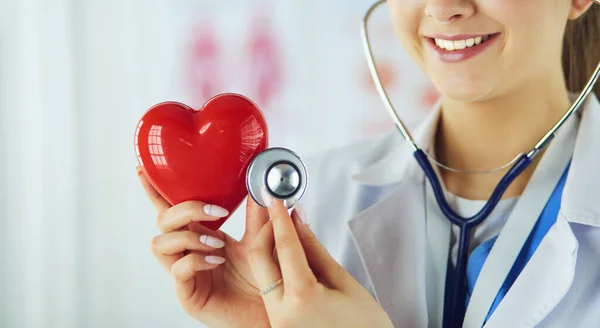 A doctor with stethoscope examining red heart, isolated on white — Stock Photo, Image