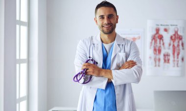 Genç ve kendinden emin erkek doktor portresi tıp ofisinde duruyor..