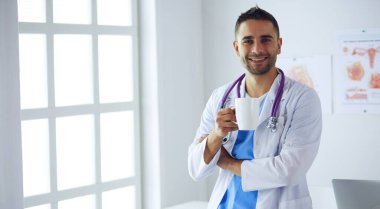 Genç ve kendinden emin erkek doktor portresi tıp ofisinde duruyor..