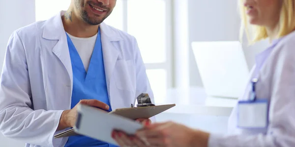 Schöner Arzt spricht mit junger Ärztin und macht sich Notizen, während er in seinem Büro sitzt. — Stockfoto