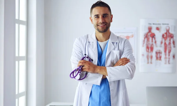 Retrato médico masculino joven y confiado de pie en el consultorio médico. — Foto de Stock