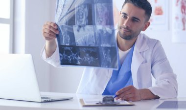 Yakışıklı doktor genç bayan hastasıyla konuşuyor ve ofisinde otururken notlar alıyor..