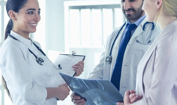 Médico bonito está conversando com jovem paciente do sexo feminino e fazendo anotações enquanto está sentado em seu escritório — Fotografia de Stock