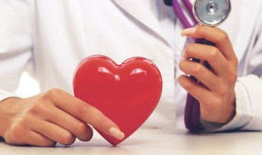 Steteskop tutan, kalbi hafif arka planda olan kadın bir doktor.