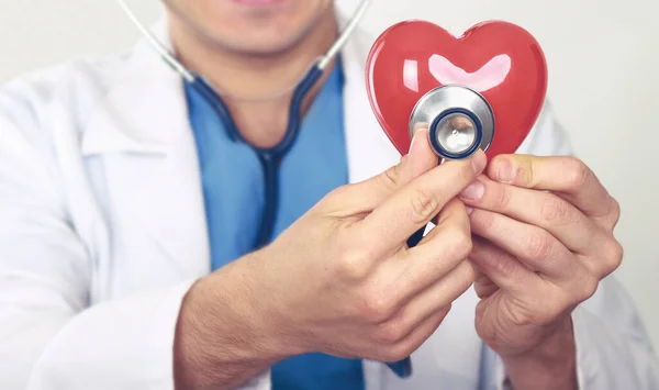 Médico com estetoscópio segurando coração, em fundo claro — Fotografia de Stock