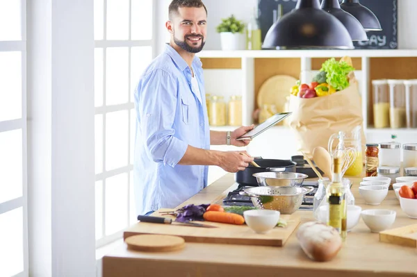डिजिटल टैबलेट पर रेसिपी का पालन करने वाला आदमी और घर में रसोई में स्वादिष्ट और स्वस्थ भोजन पकाना — स्टॉक फ़ोटो, इमेज