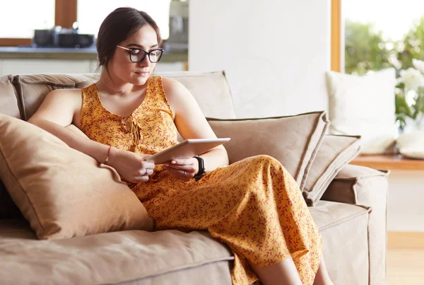 Schöne junge brünette Frau zu Hause sitzt auf Sofa oder Sofa mit ihrem Tablet-Computer und lächelt — Stockfoto