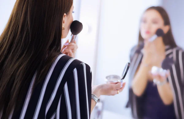 Kobieta uroda stosowania makijażu. Piękna dziewczyna patrząc w lustro i stosowanie kosmetyków z duża szczotka — Zdjęcie stockowe