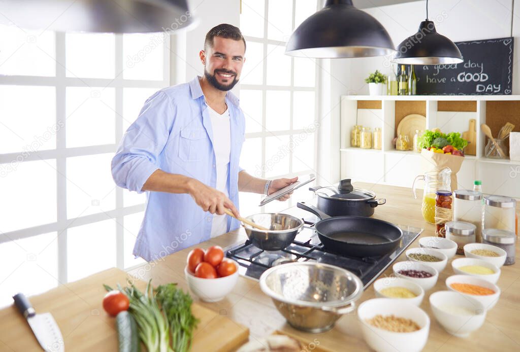 Man following recipe on digital tablet and cooking tasty and healthy food in kitchen at home