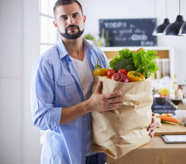 Mutfak arka planında poşet dolusu erzak tutan adam. Alışveriş ve sağlıklı gıda konsepti