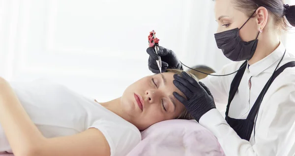 Young woman undergoing procedure of eyebrow permanent makeup in beauty salon — Stock Photo, Image