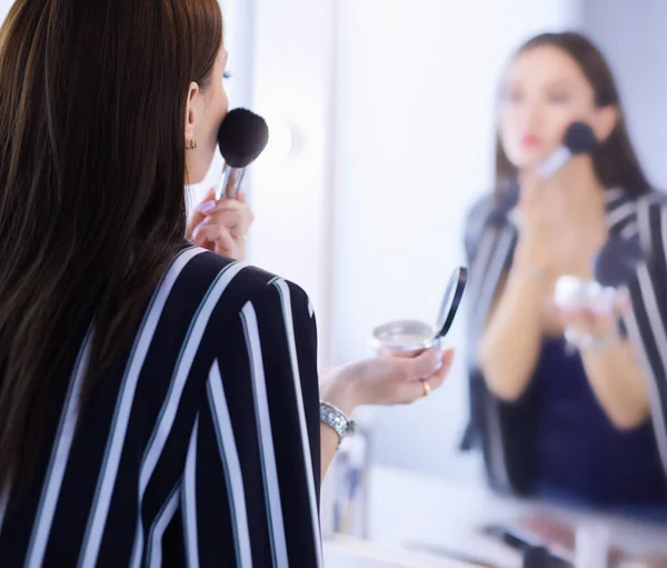 Schönheit Frau beim Schminken. schönes Mädchen, das in den Spiegel schaut und Kosmetik mit einem großen Pinsel anwendet — Stockfoto