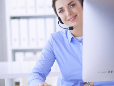 Ofisinde kulaklık takmış, telefon operatörü olarak çalışan ciddi ve güzel bir genç kadın.