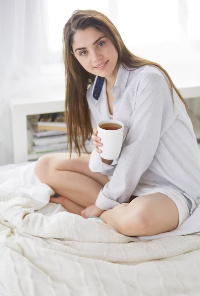 Γυναίκα που κάθεται στο κρεβάτι διαβάζοντας ένα βιβλίο και τρώγοντας πρωινό — Φωτογραφία Αρχείου