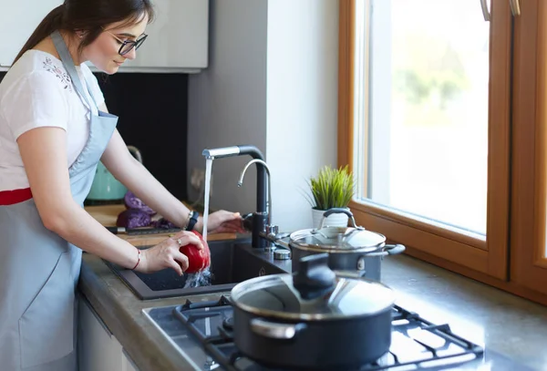 Donna che lava le verdure. Bella giovane donna che lava verdure per insalata e sorride mentre si trova in cucina — Foto Stock
