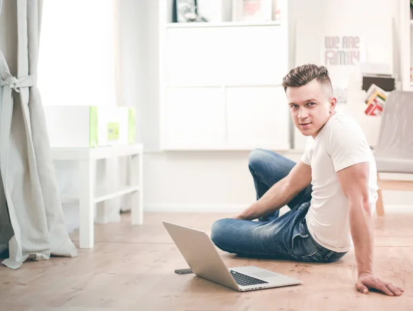 Happy young man sitting on living room floor, using laptop, smiling — Stock Photo, Image
