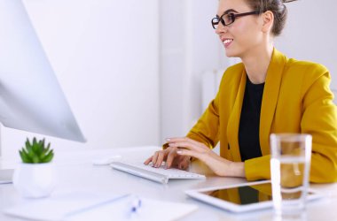 Ofis masasında çalışan ve dizüstü bilgisayarla yazan kendine güvenen genç bir iş kadını.