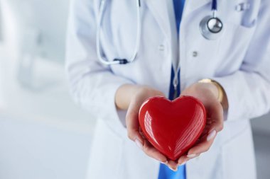 Steteskop tutan, kalbi hafif arka planda olan kadın bir doktor.