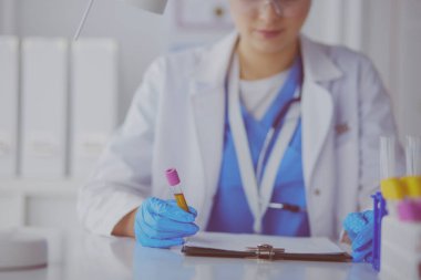 Kadın araştırmacı, beyaz arka planda izole edilmiş ilaç şişeleri ve mataralarla çevrili.
