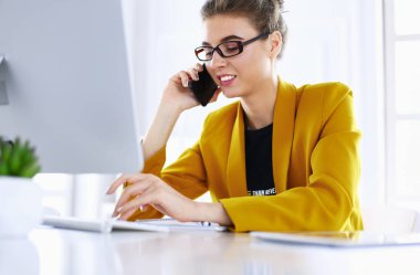 İş kadını ofiste bilgisayar ve cep telefonu kullanarak işine konsantre oluyor.