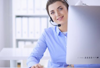 Ofisinde kulaklık takmış, telefon operatörü olarak çalışan ciddi ve güzel bir genç kadın.