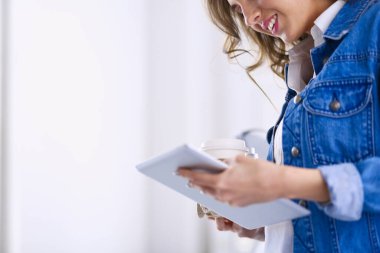 Gülümseyen kadın kahve içiyor ve kafede tablet kullanıyor.