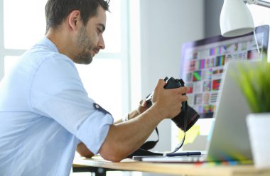 İnternette çalışırken bilgisayarın ve dizüstü bilgisayarın önünde grafik stüdyosunda oturan genç tasarımcının portresi.