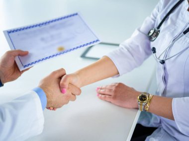 Doktor beyaz arka planda izole edilmiş bir hastayla el sıkışıyor.