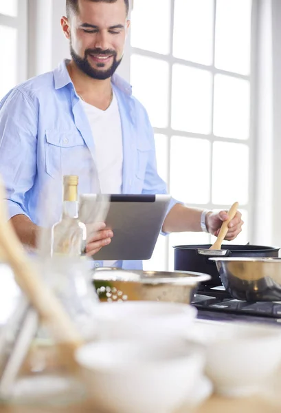 Man following recipe on digital tablet and cooking tasty and healthy food in kitchen at home — Stock Photo, Image