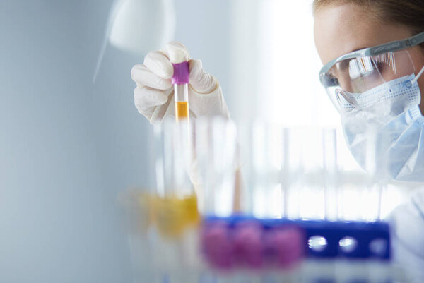 A medical or scientific researcher or doctor looking at a test tube of liquid green solution in a laboratory