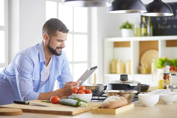 Hombre siguiendo la receta en la tableta digital y cocinar comida sabrosa y saludable en la cocina en casa — Foto de Stock