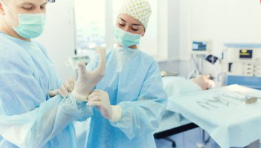 Ameliyat odasında arka planda erkek cerrah var.